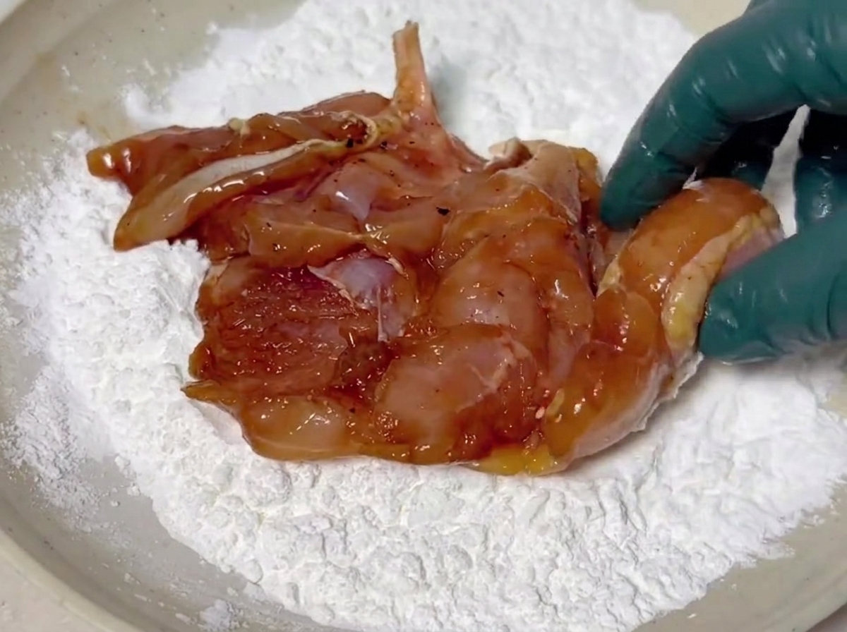 Des morceaux de poulet marinés enrobés dune couche blanche de fécule de maïs dans un plat creux.