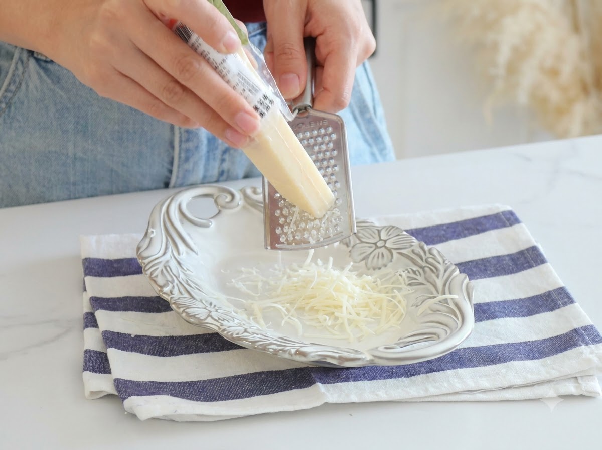 Du parmesan fraîchement râpé avec une râpe en métal sur une assiette blanche.
