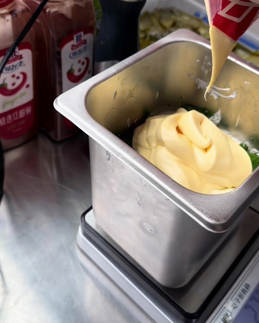 Un filet de mayonnaise jaune riche aux jaunes dœufs pressé dun sachet rouge et blanc dans le récipient en acier inoxydable contenant les ingrédients de la sauce tartare.